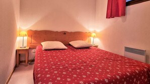 A bedroom with a wooden headboard, two bedside lamps, a red floral bedspread, and a window with a red curtain.
