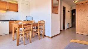 A compact kitchen with wooden cabinets, a dining table with chairs, a small TV, and a mirror on the wall.