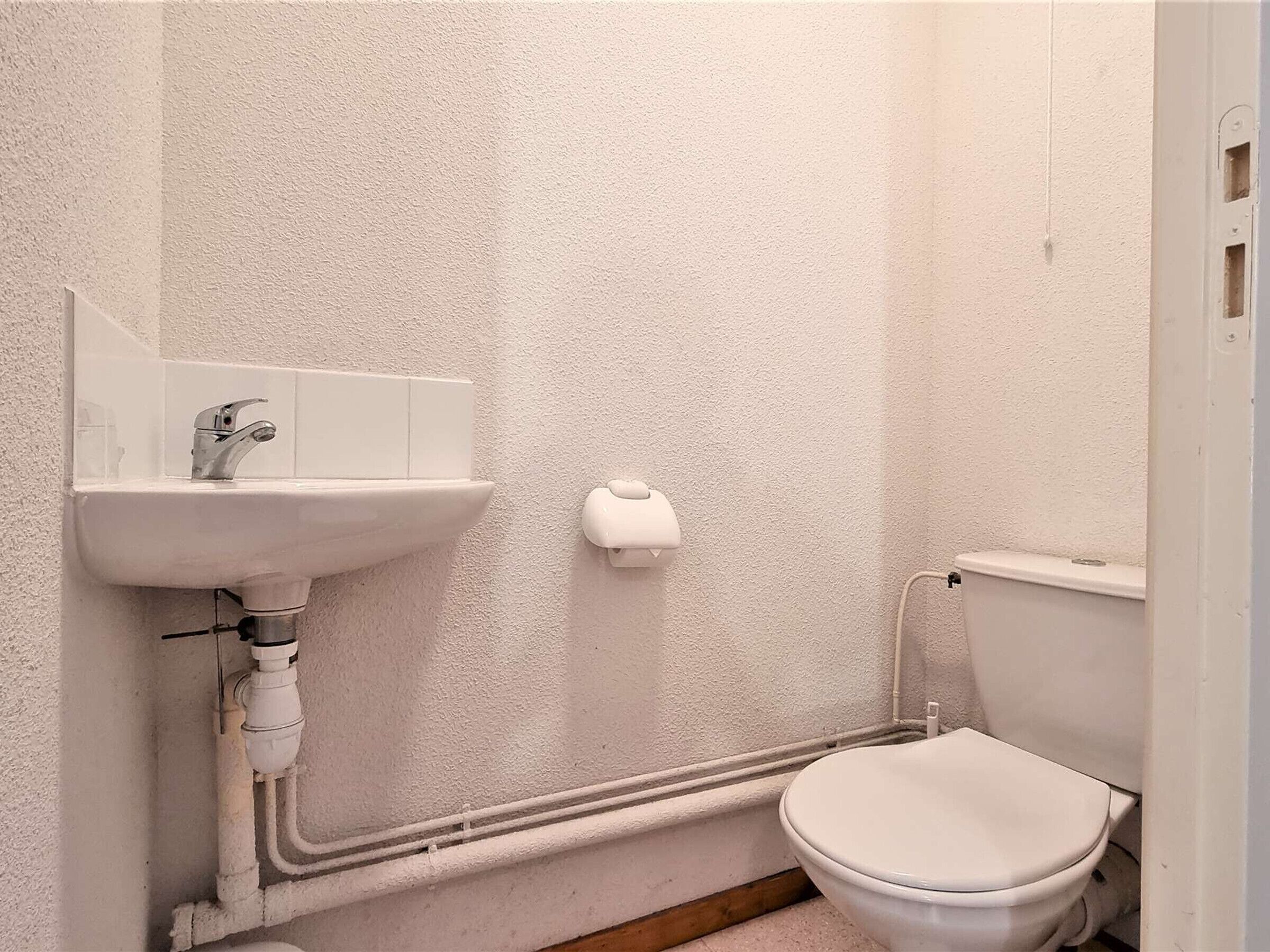 Uma casa de banho pequena e branca, com lavatório, sanita e secador de mãos.