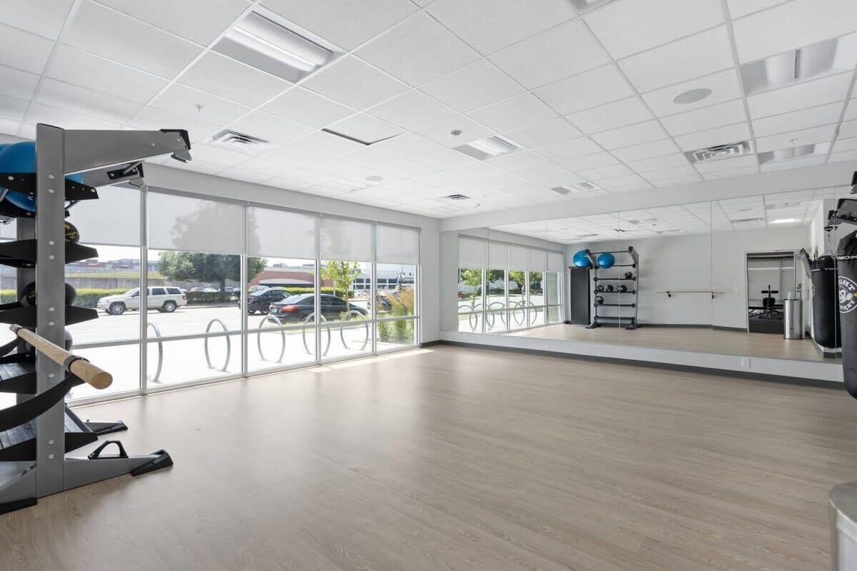 A spacious gym with large windows, exercise equipment, and a mirrored wall.