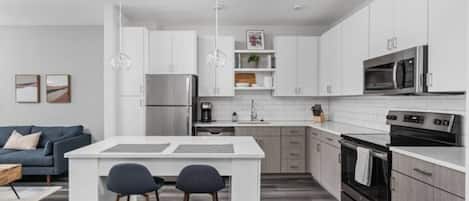 A modern kitchen with white cabinetry, a central island with stools, a built-in oven, and a microwave.