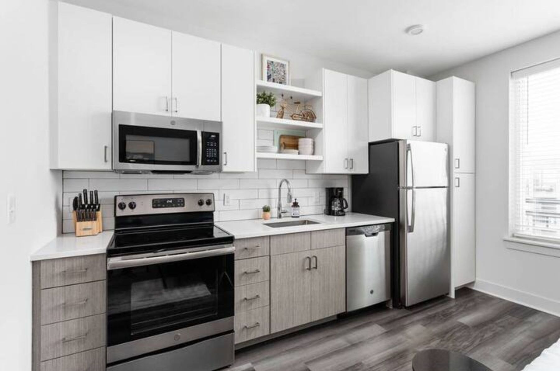 A modern kitchen with white cabinetry, a stainless steel refrigerator, a microwave, and an oven.