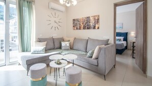 A modern living room with a grey sectional sofa, two round coffee tables, and a large abstract painting on the wall. - Alcmene Lux Apartment (Zakynthos)