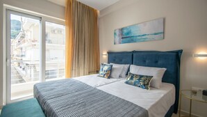 A hotel room with a large bed, a view of a building through a window, and a painting on the wall. - Alcmene Lux Apartment (Zakynthos)