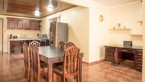 A spacious kitchen with a dining area, wooden cabinets, a refrigerator, and a clock on the wall.