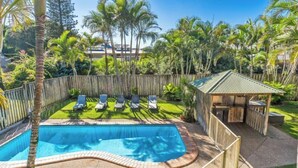 A swimming pool surrounded by a wooden fence, with lounge chairs and a gazebo. - Bayside Court - Three Bedroom (Byron Bay)