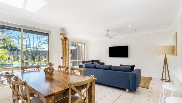 A modern living room with a wooden dining table, blue sofa, and a flat-screen TV mounted on the wall. - Bayside Court - Three Bedroom (Byron Bay)