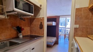 A compact kitchen with a microwave, sink, and a small dining area with a bench and table. - Cozy studio for 4 with terrace, near slopes and shops (Le Dévoluy)
