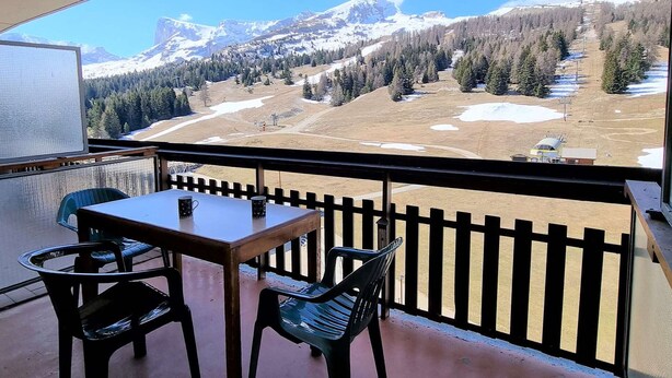 A balcony with a table and chairs, overlooking a mountainous landscape with snow patches and a ski slope. - Cozy studio for 4 with terrace, near slopes and shops (Le Dévoluy)