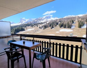 Un balcone con tavolo e sedie, affacciato su un paesaggio montano con chiazze di neve e una pista da sci.