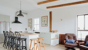 A modern kitchen with a central island, bar stools, and a dining area with a leather chair. - Massinger Views Byron Bay (Byron Bay)