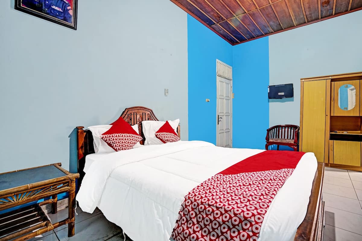 Una habitación con cama, armario de madera, silla y una mesita.