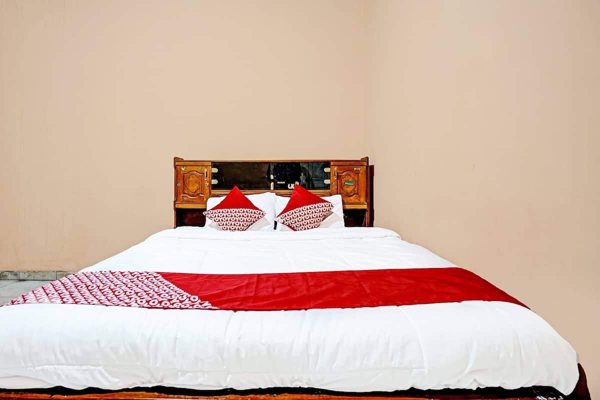 Una cama con una colcha blanca y roja, dos almohadas rojas y un cabecero de madera con un espejo.