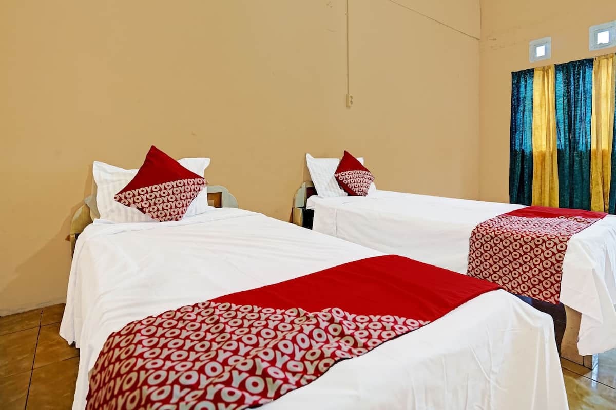 Una habitación de hotel con dos camas, cada una con una colcha blanca y almohadas rojas.
