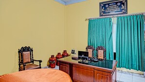 Een kamer met een bed, een bureau met een computer en een stoel. Op het bureau staan decoratieve vazen en er hangt een gordijn met een patroon.