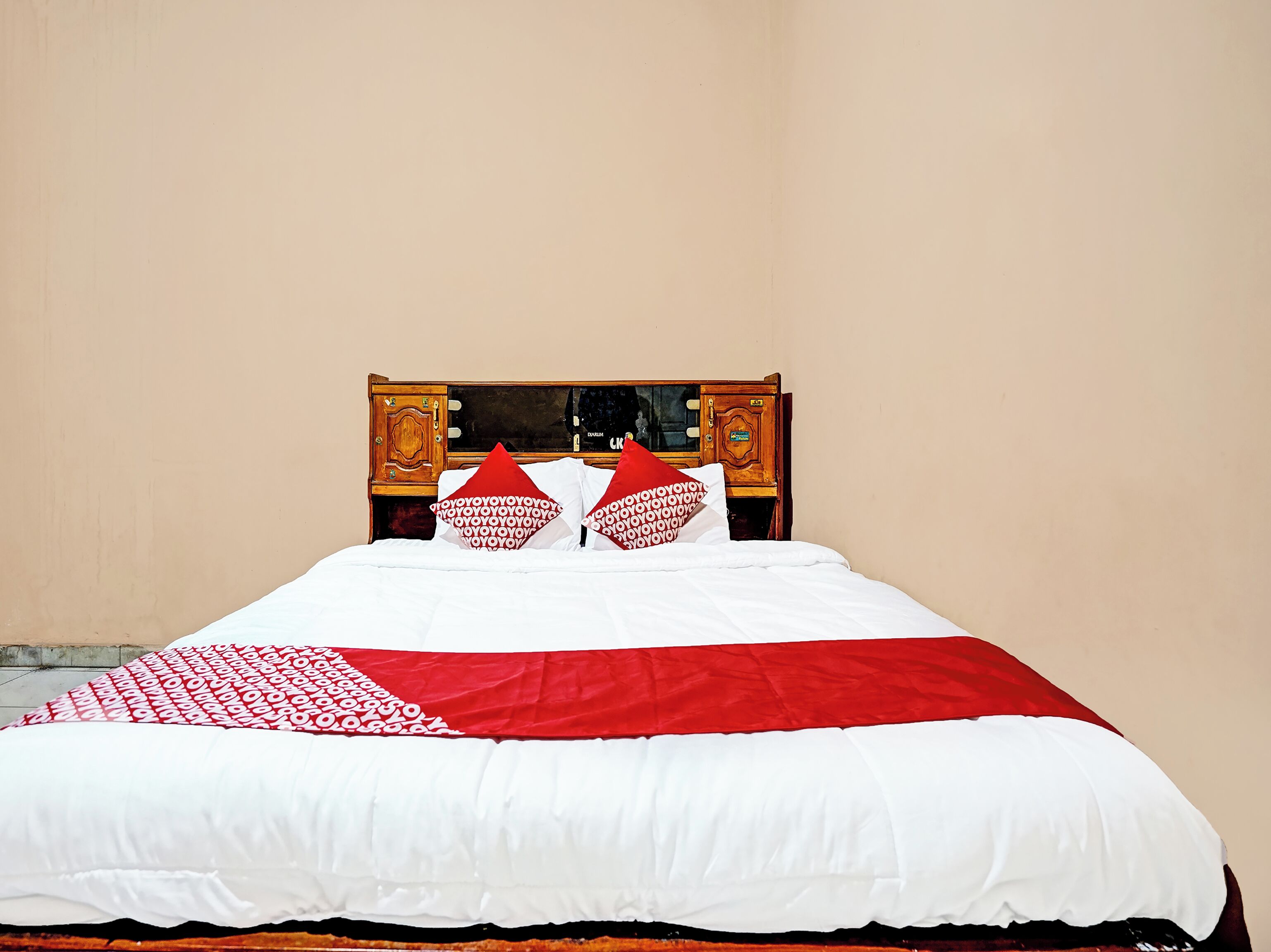 Una cama con ropa de cama blanca y roja, un cabecero de madera y un pequeño mueble de madera con espejo.