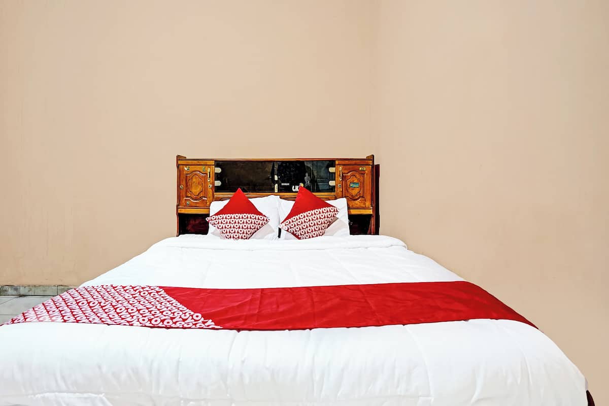 Una cama con ropa de cama blanca y roja, un cabecero de madera y un pequeño mueble de madera con espejo.