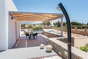 Eine überdachte Terrasse im Freien mit Tisch und Stühlen, einer Steinmauer und einem Pool.