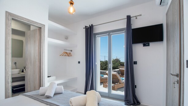 Quarto moderno com cama, banheiro com pia e vista para móveis de exterior através de uma porta de vidro.