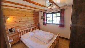 A wooden room with a bed, a window with curtains, and a small shelf. - Chalet 'Le Chandeley' with Private Terrace, Private Garden and Wi-Fi (Champdray)