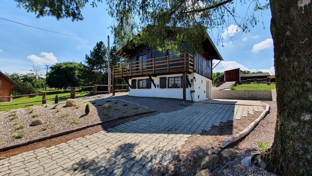 A wooden cabin with a balcony, surrounded by a gravel path and a small garden.