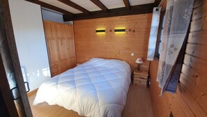 A wooden room with a bed, a nightstand, and a wall-mounted lamp.