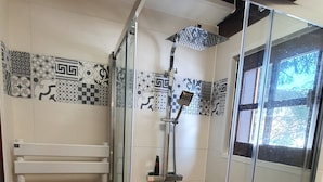 A glass-enclosed shower with a handheld showerhead, a white towel rack, and patterned tiles on the walls.