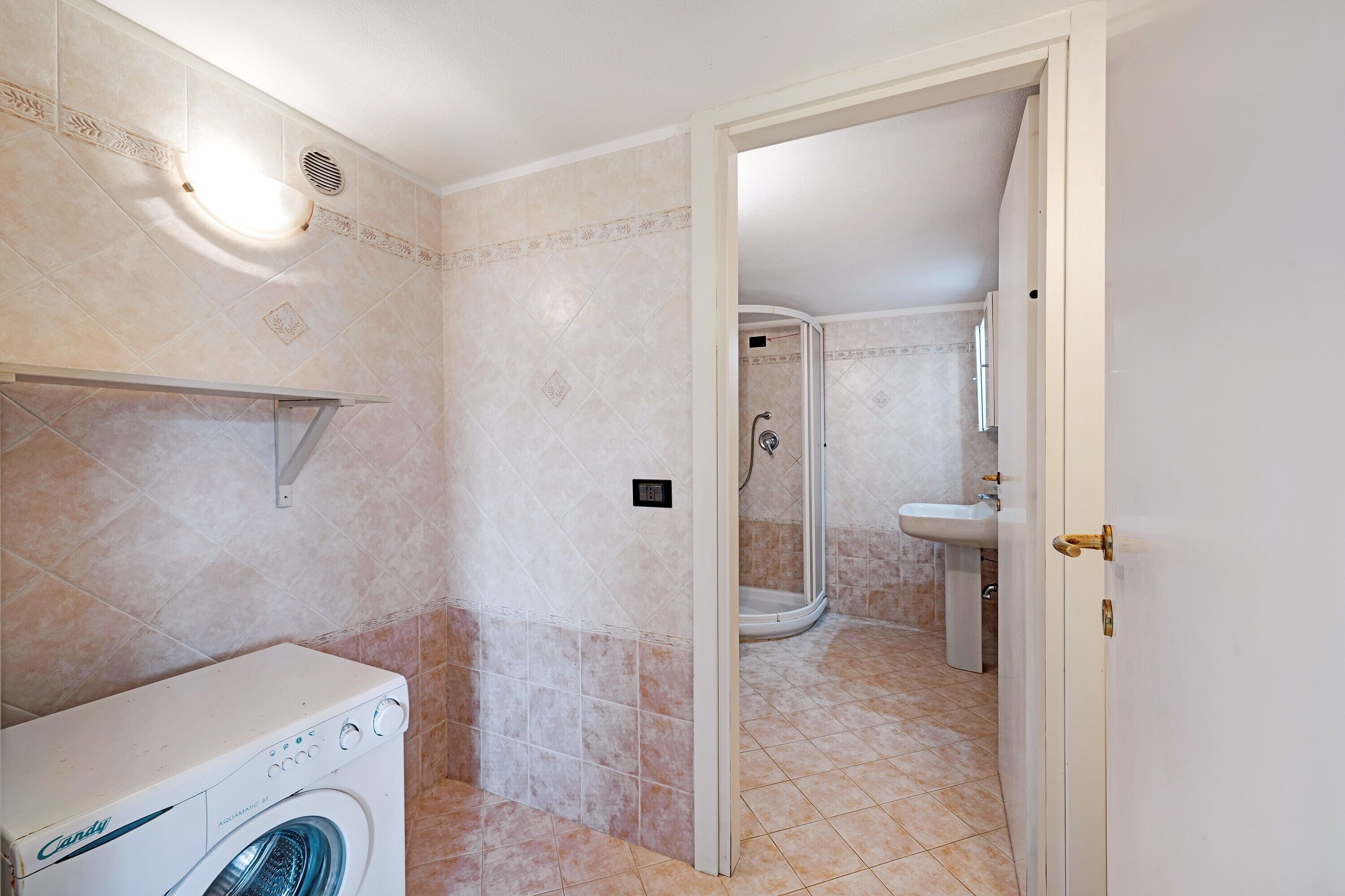 A bathroom with a washing machine, a shower, and a sink.
