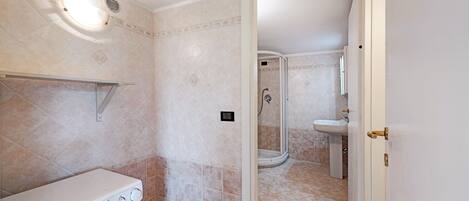 A bathroom with a washing machine, a shower, and a sink.