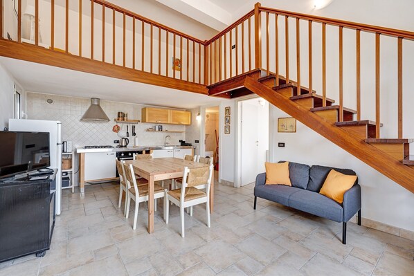 A modern kitchen with a dining area, a staircase, and a living room with a sofa.
