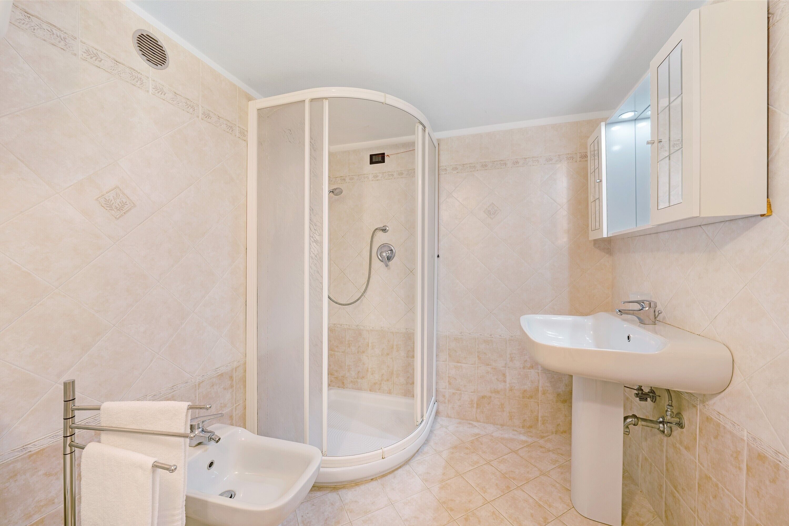 Un baño con ducha, lavabo y toallero.