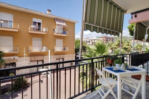 A balcony with a table and chairs, a railing, and a view of a building with balconies.