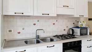 A kitchen with white cabinets, a double sink, a stove, a microwave, and a dishwasher. - Apartment 'Mari Fior' with Sea View, Balcony and Wi-Fi (San Bartolomeo)