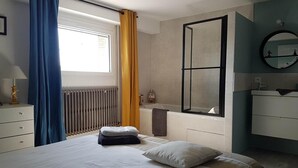 Une chambre à coucher avec un lit, un radiateur, une fenêtre avec des rideaux, un miroir et une commode.
