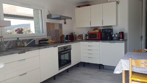 Une cuisine compacte avec des meubles blancs, un four encastré, un four à micro-ondes et un coin repas comprenant une table et des chaises.