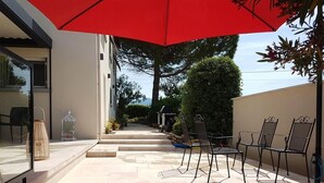 Une terrasse avec des sièges, un parasol rouge et une porte vitrée donnant sur une pièce.