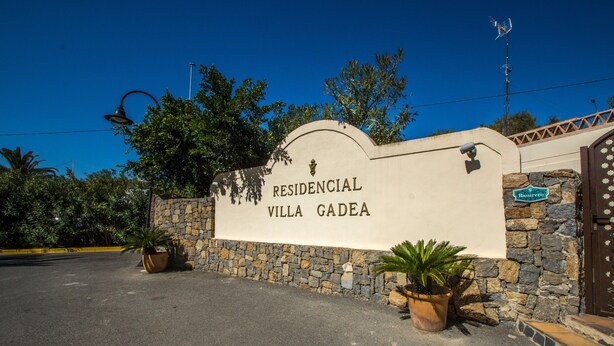 A sign for 'RESIDENCIAL VILLA GADEA' with a stone wall and potted plants.