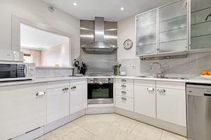 Una cocina moderna con armarios blancos, electrodomésticos de acero inoxidable, un reloj y un lavavajillas.