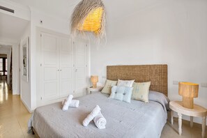 Une chambre à coucher avec un grand lit, une tête de lit en osier, deux tables de chevet avec des lampes et une armoire blanche.
