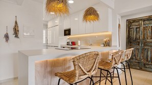 A modern kitchen with a central island, bar stools, hanging wicker light fixtures, and a rustic wooden door. - Villa Gadea 7-2 Apartment with Sea Views, Wi-Fi, and Air Conditioning (Altea)