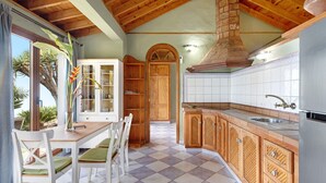 Une cuisine avec un plafond en bois, un sol carrelé et une vue sur l’extérieur.