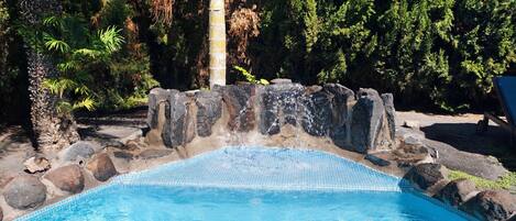 Une piscine à l’eau d’un bleu cristallin, entourée de rochers et d’arbres.