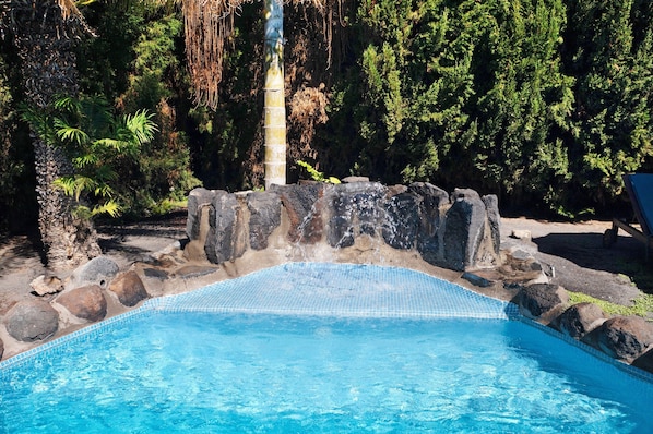 A swimming pool with clear blue water, surrounded by rocks and trees.