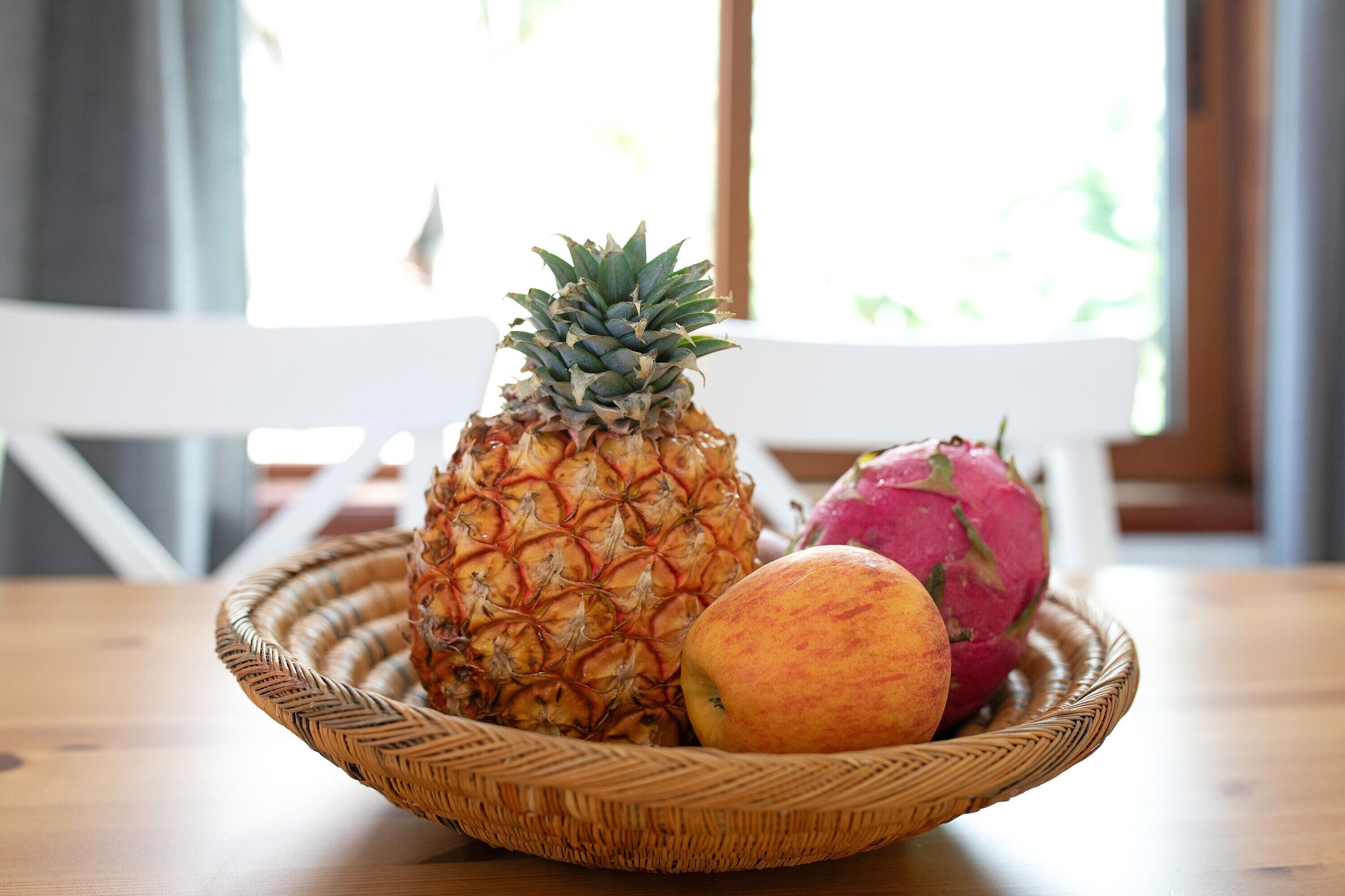 En fletkurv med frugt på et træbord, hvor der er en ananas, pitahaya og en pære.