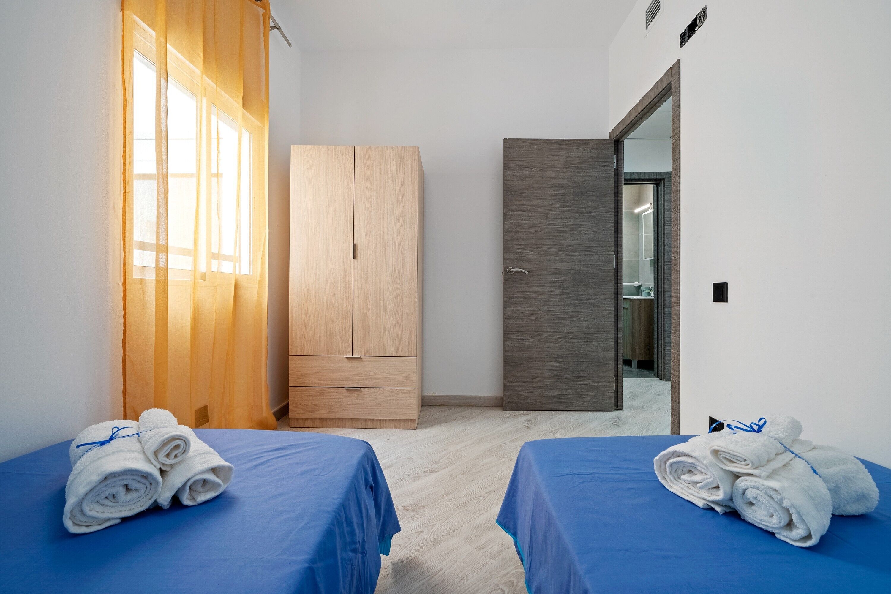 A hotel room with two beds, a wooden wardrobe, a mirror, and a bathroom visible through a glass door.