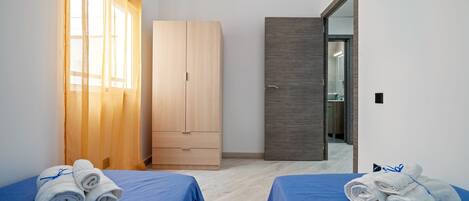 A hotel room with two beds, a wooden wardrobe, a mirror, and a bathroom visible through a glass door.