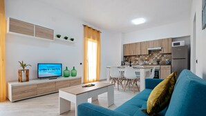 A modern living room with a sofa, coffee table, TV, and a kitchen area with cabinets and appliances.