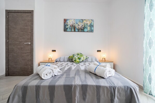 A hotel room with a bed, two bedside lamps, a painting on the wall, and a door.