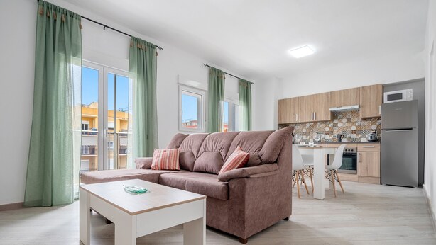 Una sala de estar con sofá, una mesa y una cocina al fondo.