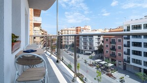 Un balcón con una mesa y sillas, con vistas a un paisaje urbano que incluye edificios y una calle.
